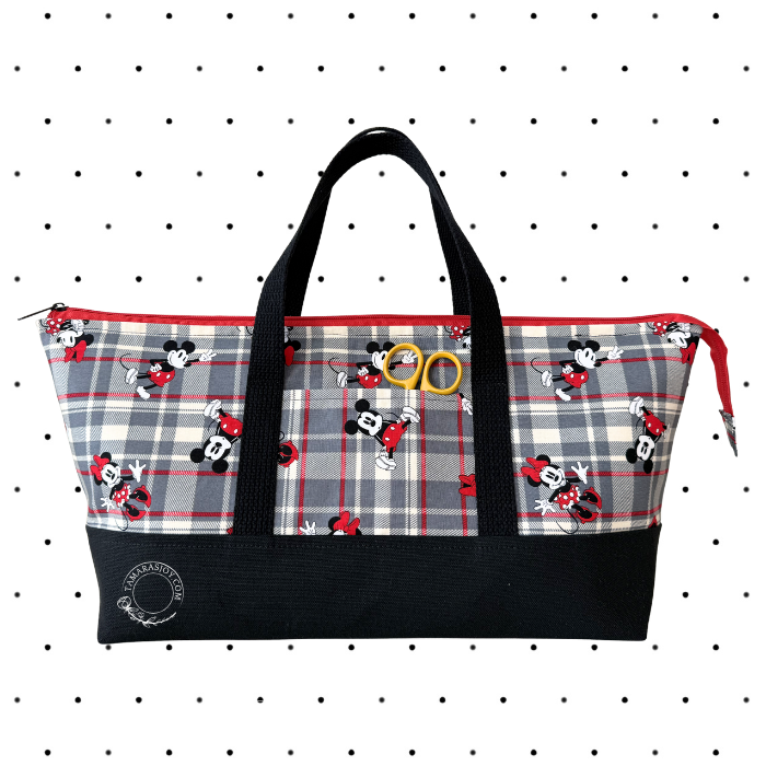 A Disney tote bag featuring a gray and red plaid pattern with Mickey and Minnie Mouse prints, black handles and bottom panel, and two yellow metal rings on the front.